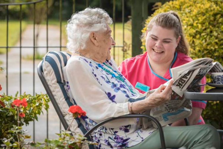 Dementia care home resident reading newspaper with care giver